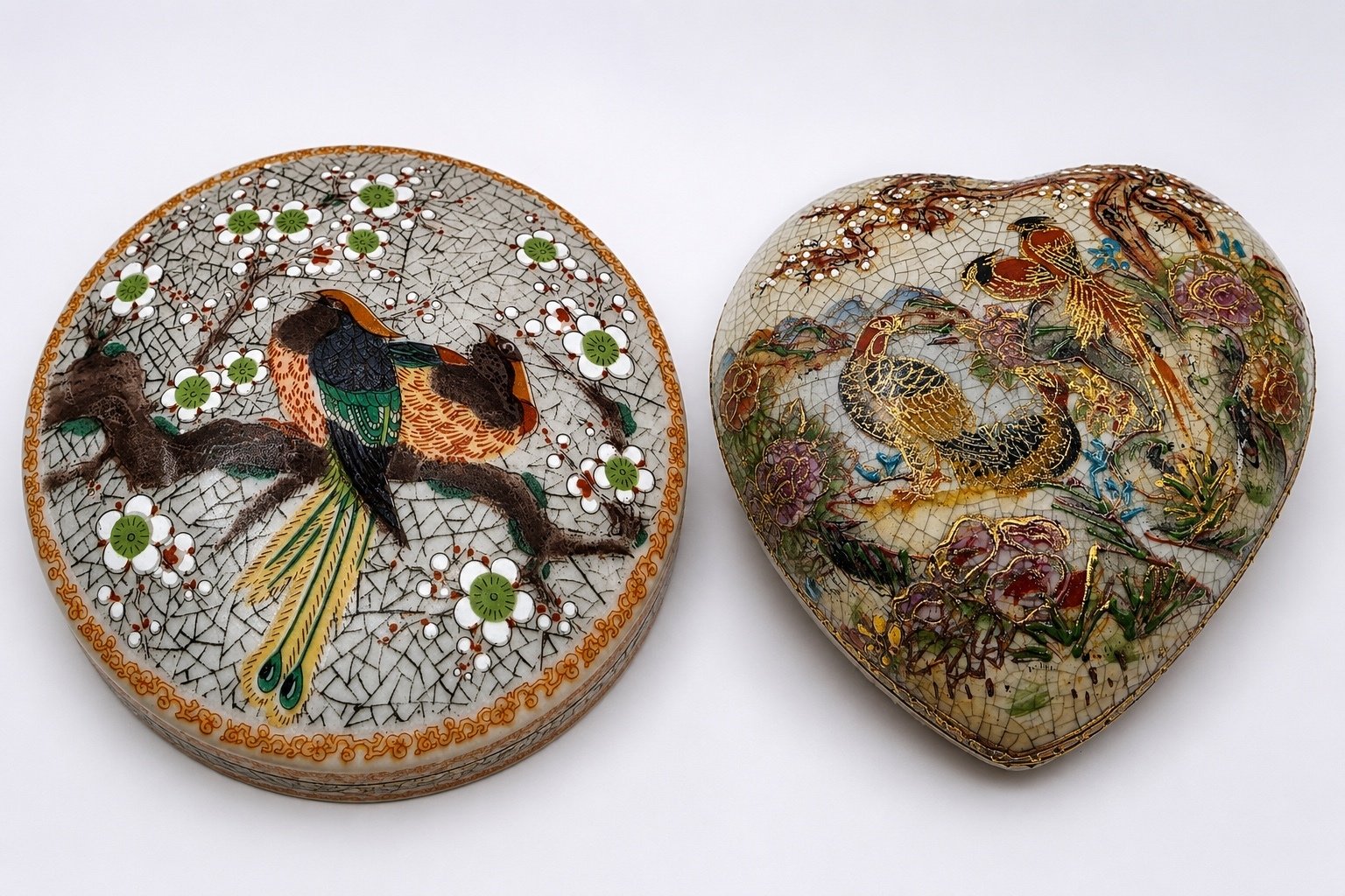 Top view of two Satsuma-style porcelain trinket boxes: round bird box and heart-shaped box with painted birds, floral glaze.
