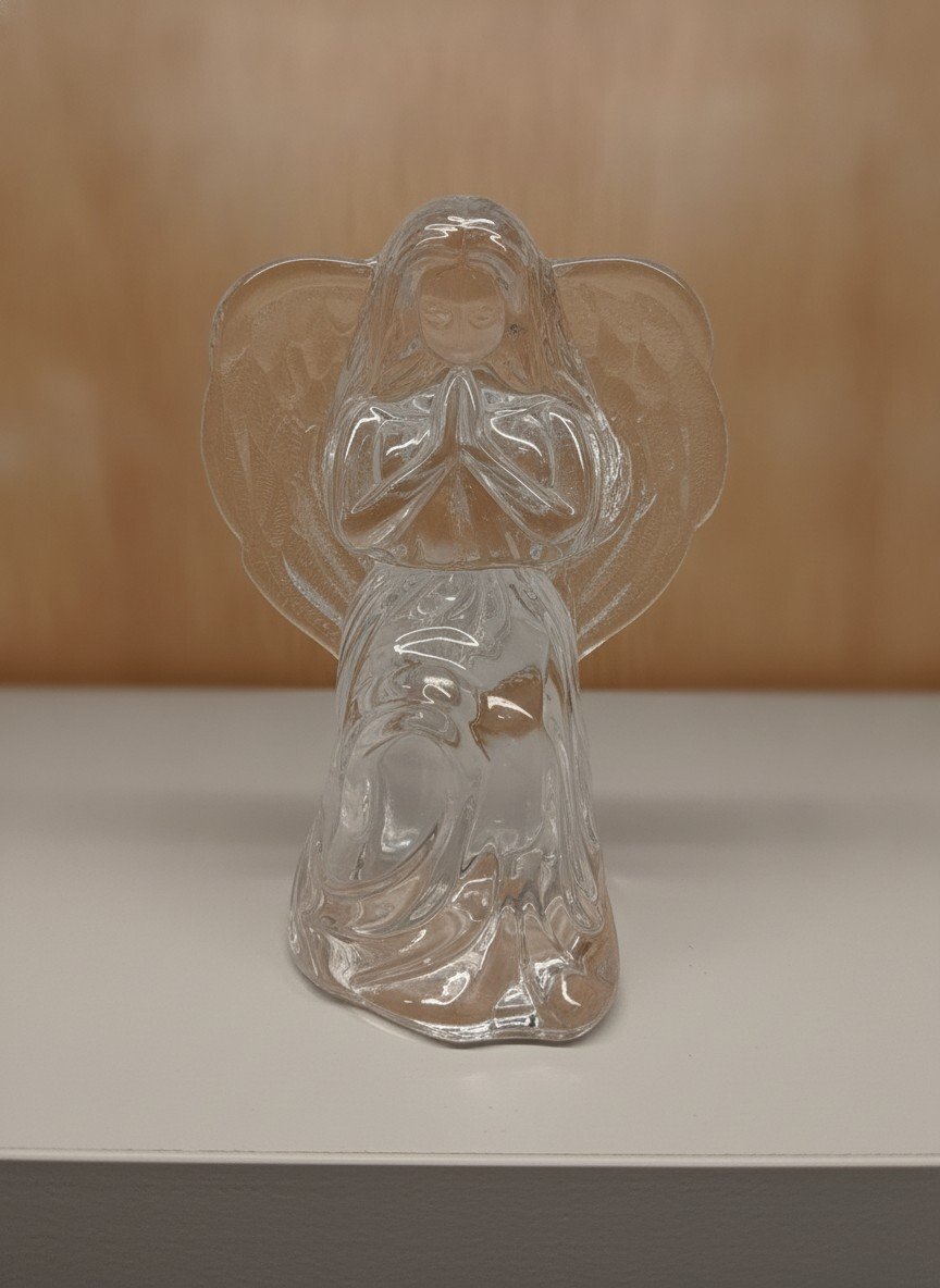 Clear crystal praying angel figurine, front view showing kneeling figure with folded hands, textured wings and flowing robe on a flat surface.