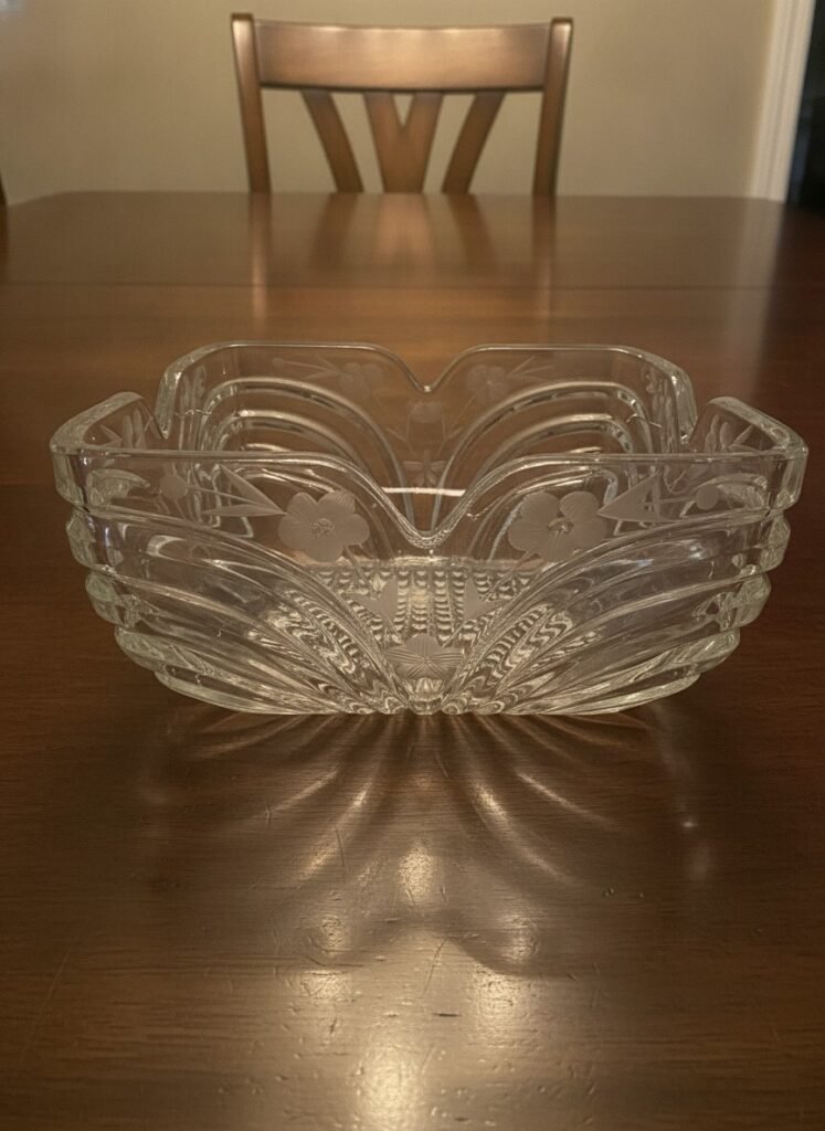 Clear pressed glass square console bowl, front view showing scalloped corners, ribbed panels and waffle-pattern center on a wood table