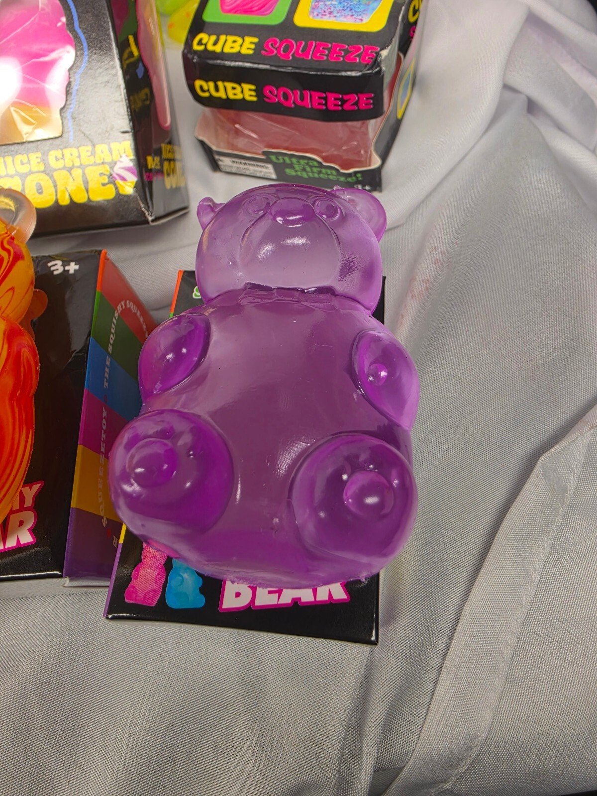 Top view of a translucent purple gummy bear squishy displayed on fabric, showing rounded paws and slightly glossy surface.