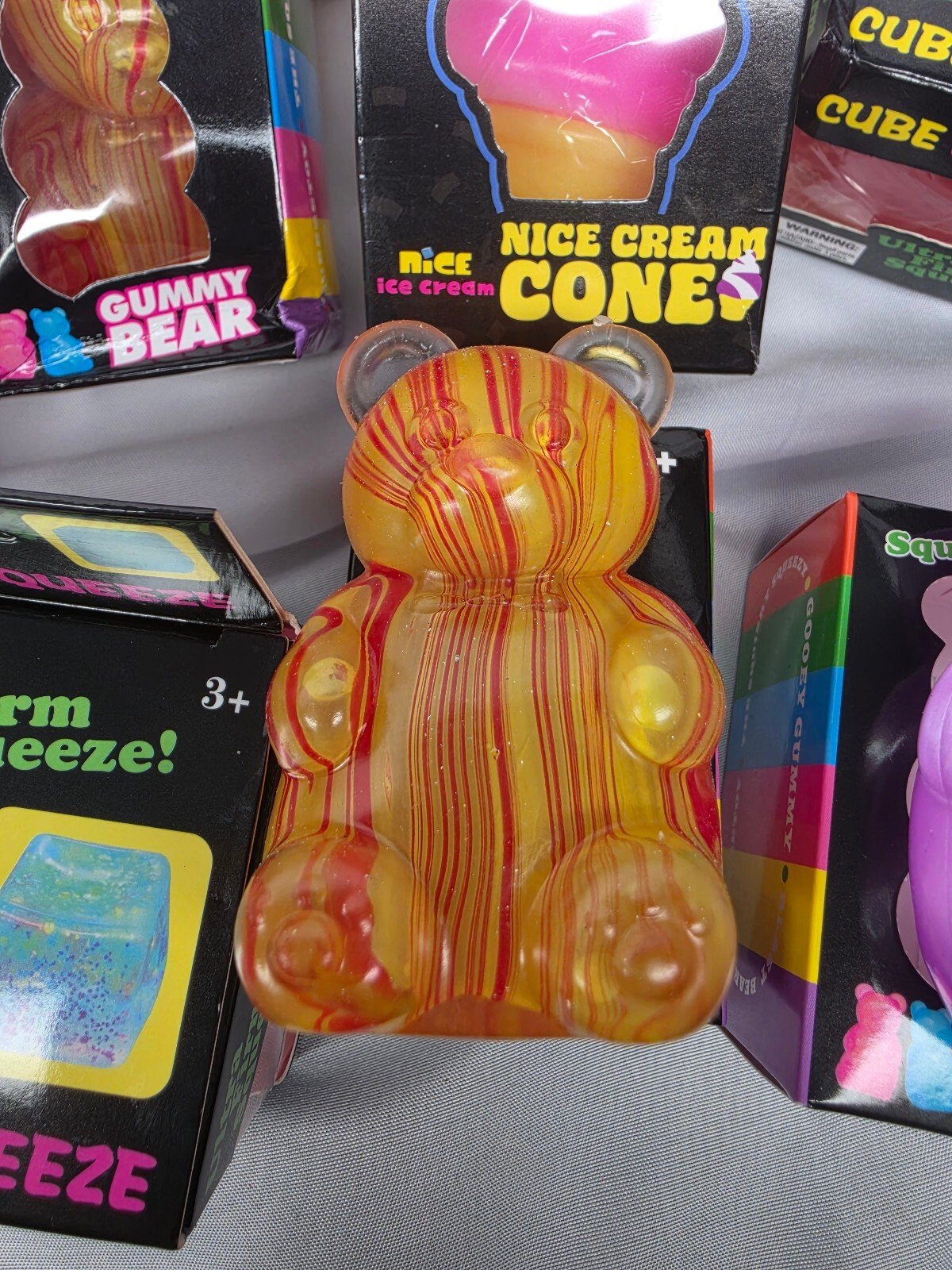 Close-up of a marbled orange-and-red translucent gummy bear squishy standing upright in front of boxed packaging.