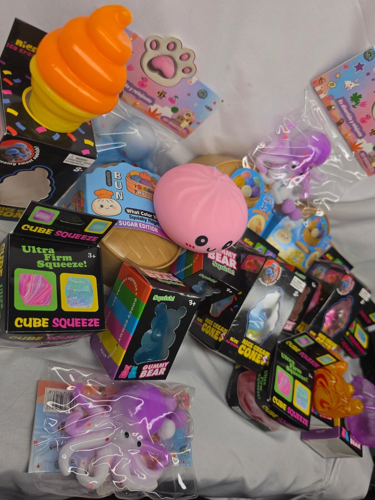 Overhead assortment showing multiple boxed squishies and loose toys including an orange ice-cream cone, pink bun, octopus and cube-squeeze boxes.