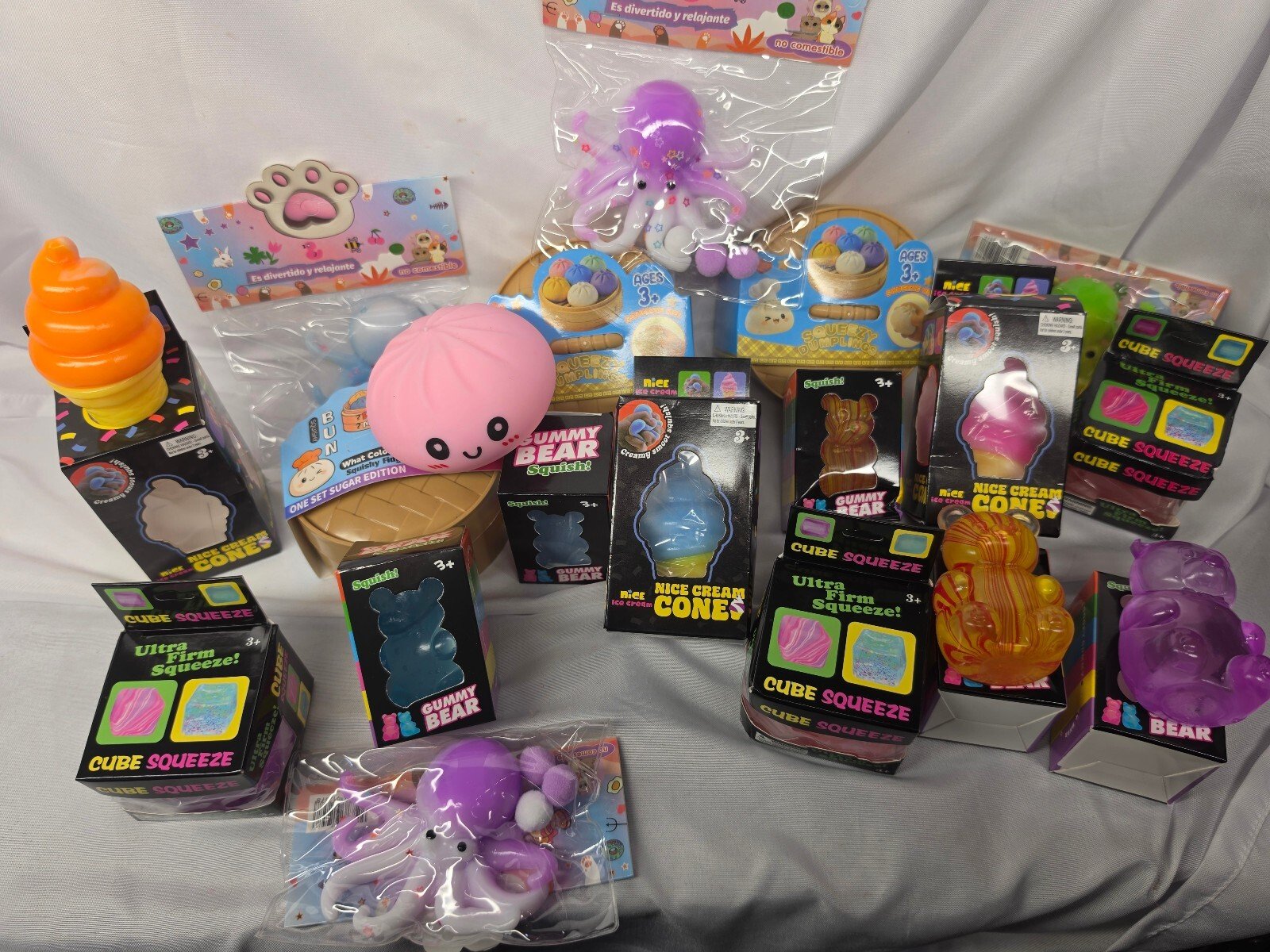 Display of full assortment with a packaged purple octopus squishy, buns, gummy bears, cube squeeze boxes and other loose toys.