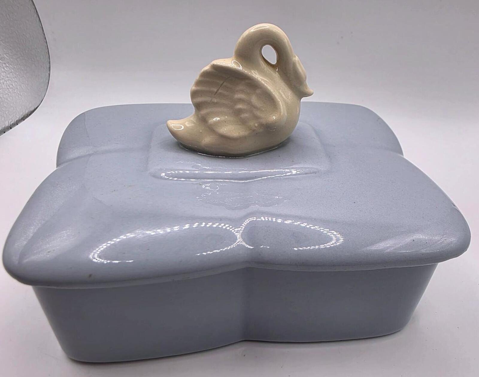 Close-up top view of a glossy gray rectangular trinket box lid with a small cream-colored sculpted swan handle.