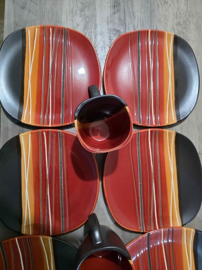 Top-down view of four square red, orange, black and white striped stoneware plates arranged around a matching mug.