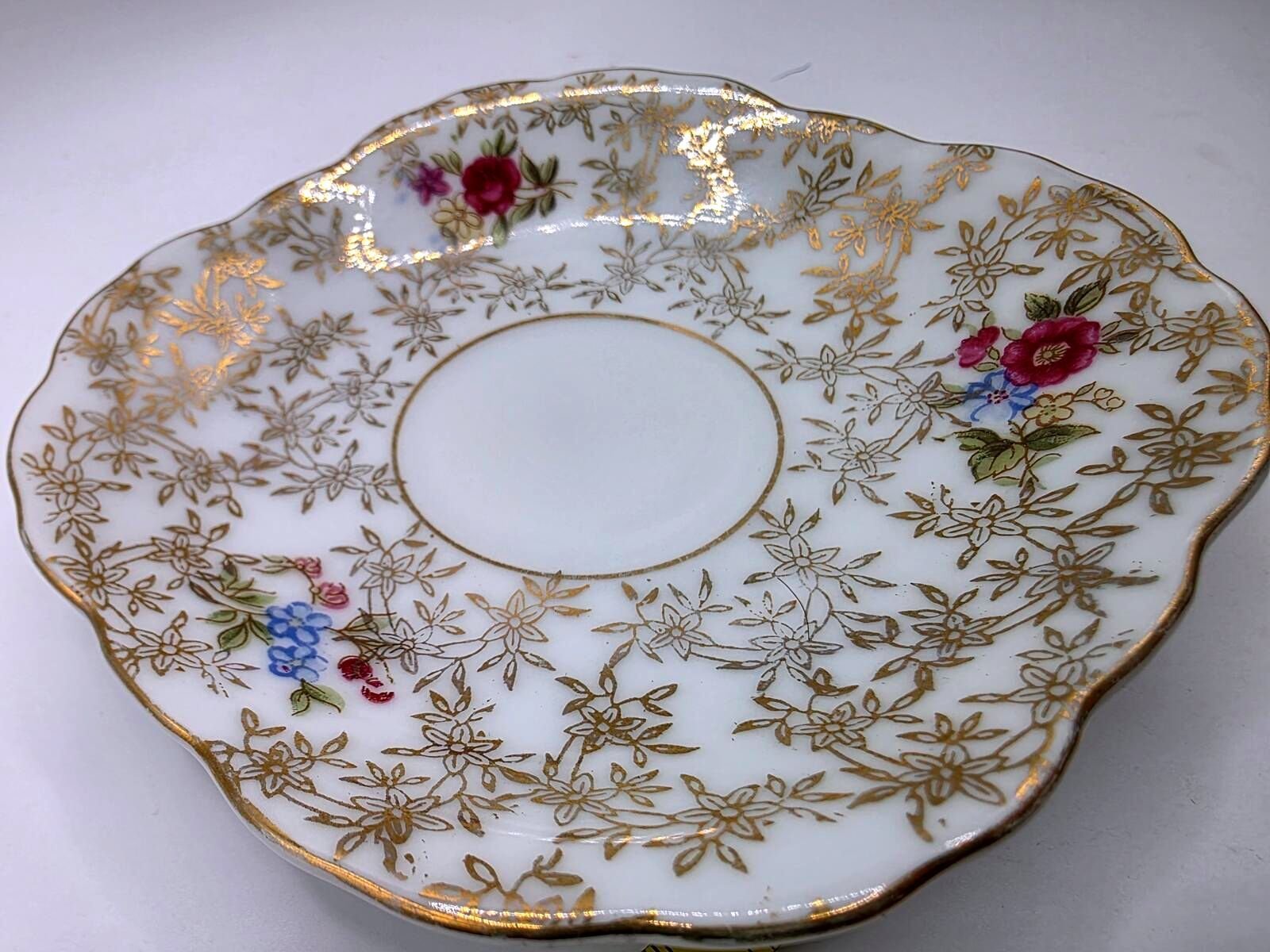 Close-up angled view of Lefton porcelain saucer showing gold floral lattice pattern, colorful hand-painted blossoms and scalloped gilt rim.