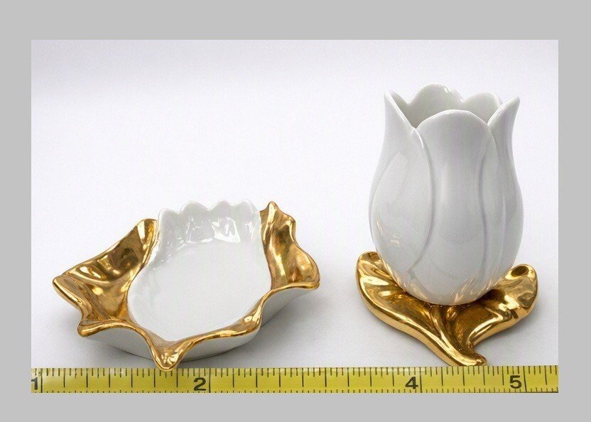 White porcelain tulip bud vase on gold-tone leaf base beside matching white leaf-shaped dish; ruler visible at front.