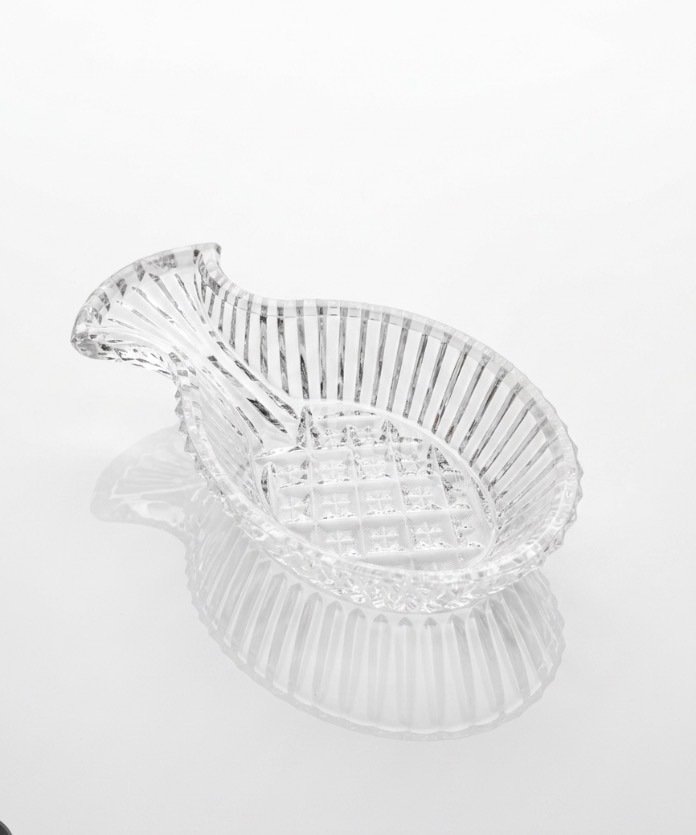 Clear pressed-glass pineapple spoon rest with vertical ribbing, diamond-point center and scalloped edge, angled view.