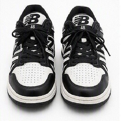 Front/top view of black-and-white New Balance low-top sneakers showing perforated white toe boxes, black leather overlays, laces, and NB tongue logos.