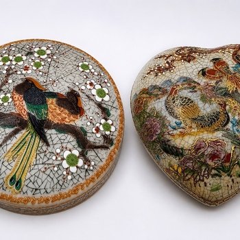 Close detail of heart-shaped Satsuma-style trinket box with gold-accented birds and floral decoration beside round bird box.