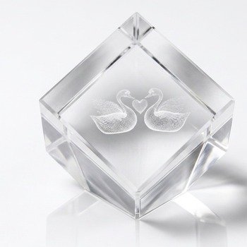 Top-angled view of clear faceted paperweight showing etched swans with heart shape between necks and reflected shadow.