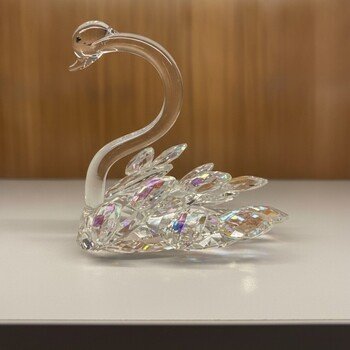 Three-quarter front view of clear lead crystal swan highlighting faceted AB wing accents and polished body on a shelf.