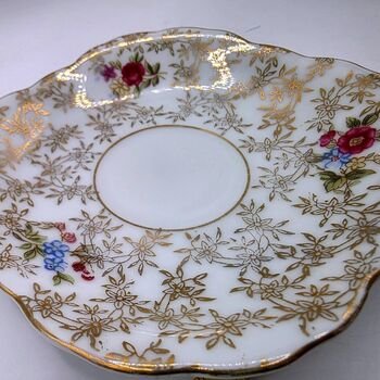 Angled top view of Lefton 4.5in porcelain saucer showing central cup well, gold floral lattice and hand-painted red and blue flower accents.