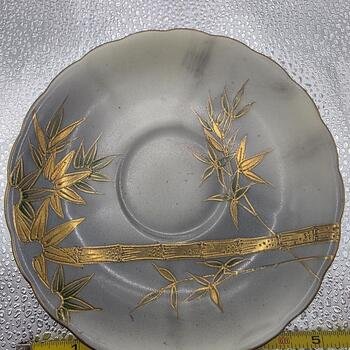 Top view of gray porcelain saucer with gold bamboo moriage pattern, scalloped edge and shallow center cup indent.