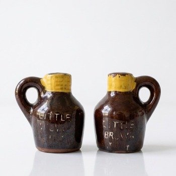 Front view of two Little Brown Jug ceramic shakers showing handles, yellow necks and worn lettering on glossy brown glaze